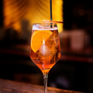 Verre de cocktail Spritz rafraîchissant servi avec des glaçons, une tranche d'orange et une paille sur un comptoir de bar