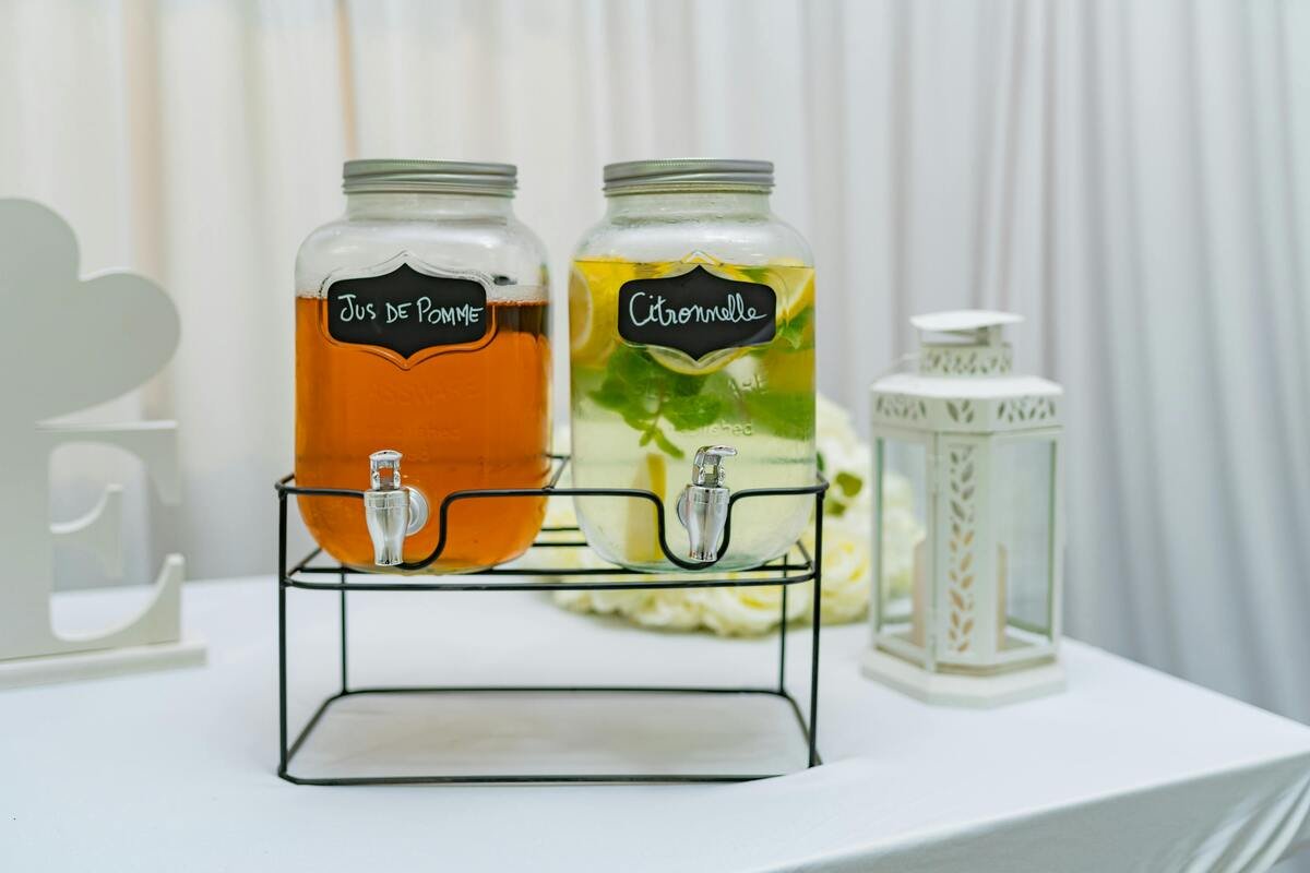 Lifestyle : Une table de réception avec deux verres. Un grand verre type Virgin Mojito avec glaçons, et à côté un verre de jus de pomme trouble, devant une belle fontaine 3L.