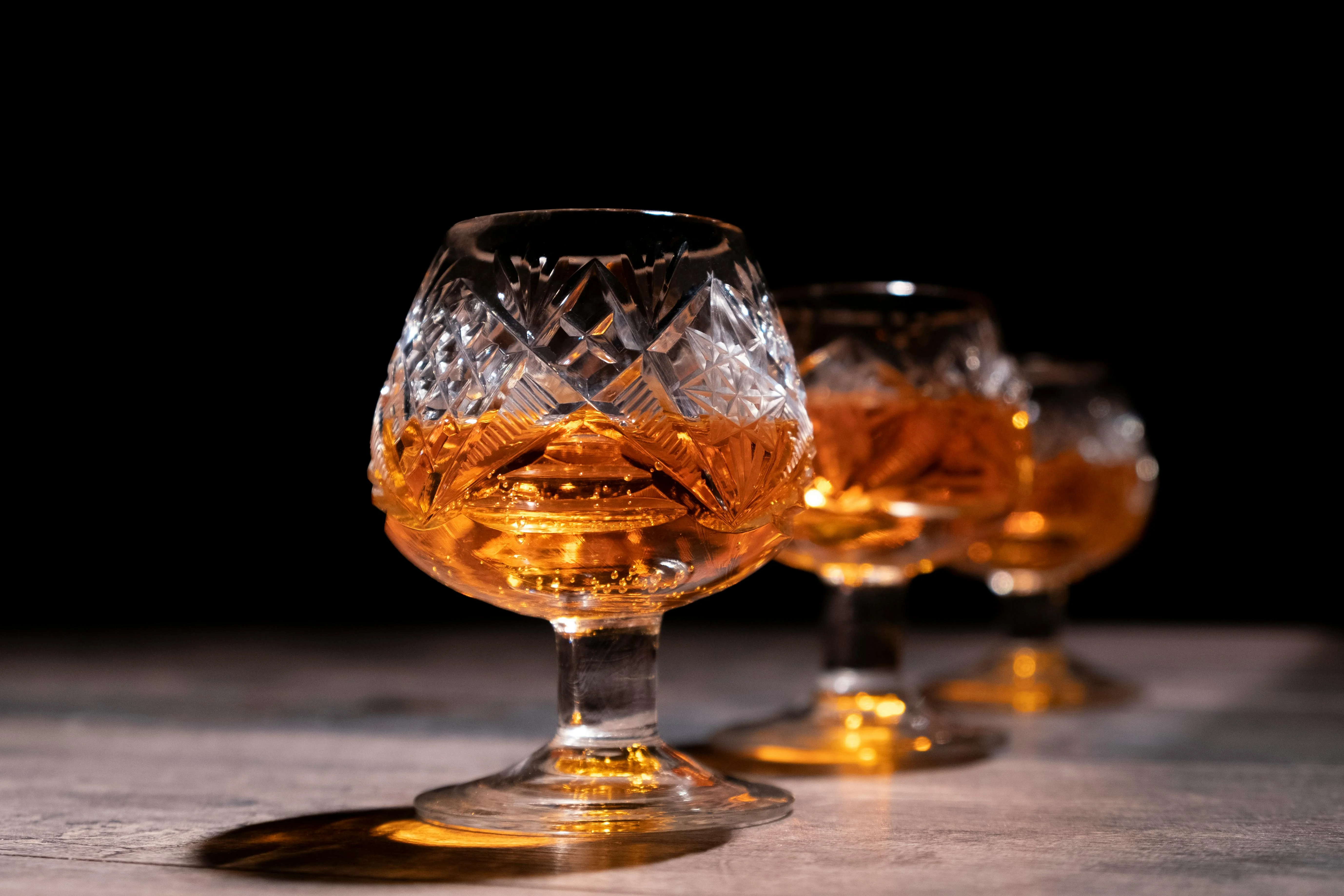 Verres de dégustation en cristal contenant un spiritueux ambré, photographie de luxe sur fond noir